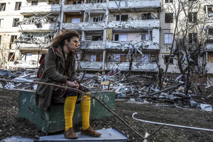 Una mujer permanece sentada frente a un edificio dañado por ataques rusos en Kiev, capital de Ucrania.